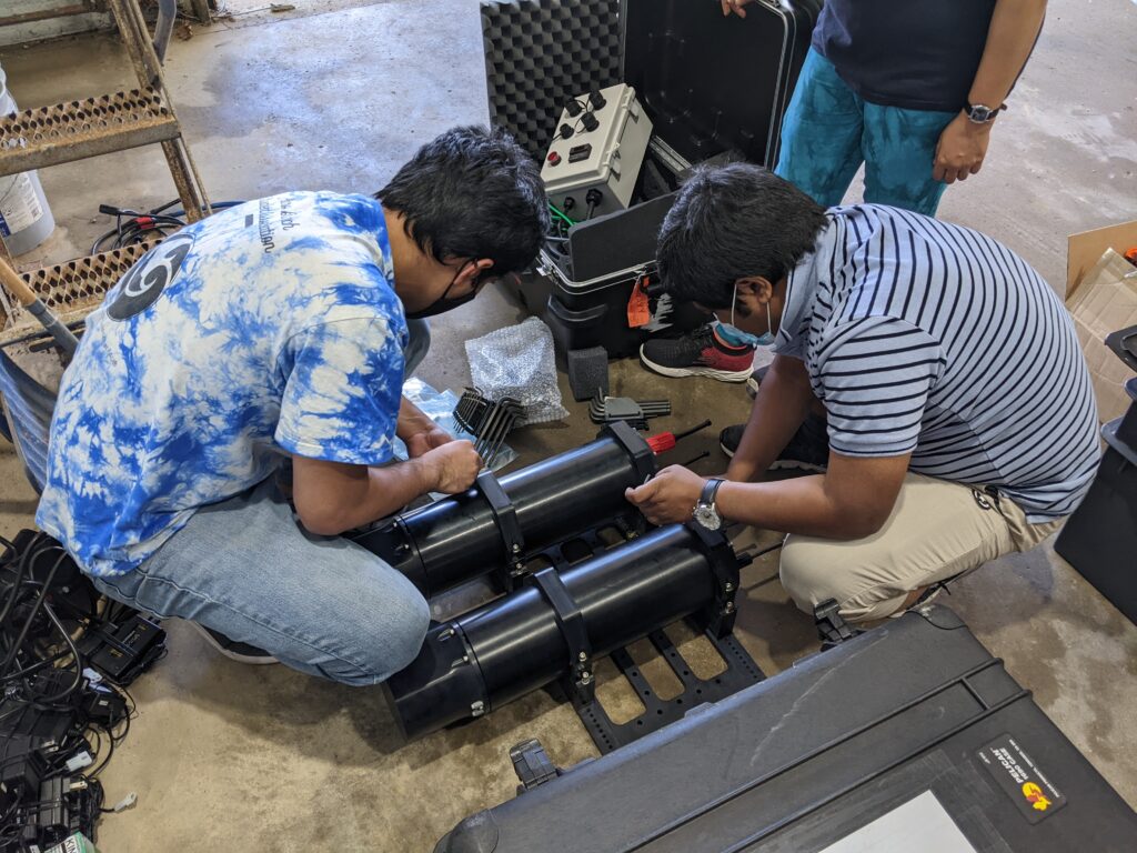 Two people work on device made of two black cylinders.
