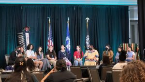 A dozen young people sit on a conference stage.