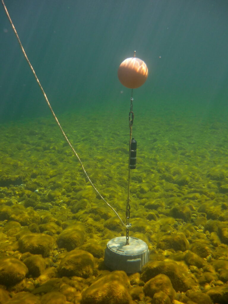 A concrete anchor is cabled to an orange float. A black device is bolted to the connecting cable. 