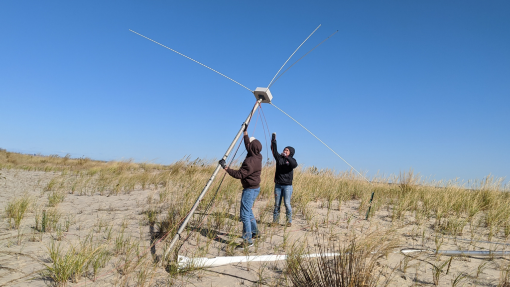 Two people on a beach install a large antenna.